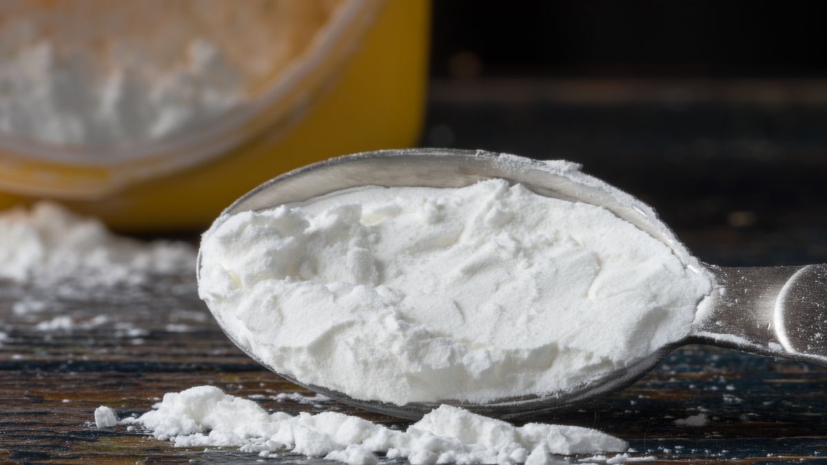 Egy evőkanál kukoricakeményítő, háttérben egy üveg tárolóval.